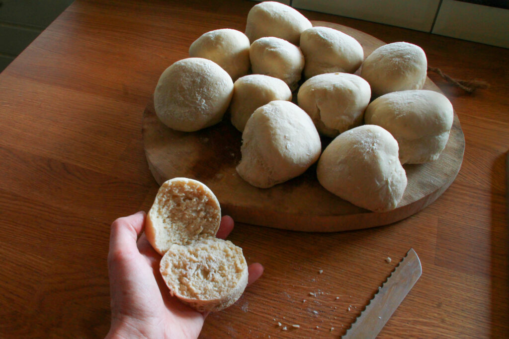 Hand met opengesneden broodje. Versgebakken broodjes op houten plank